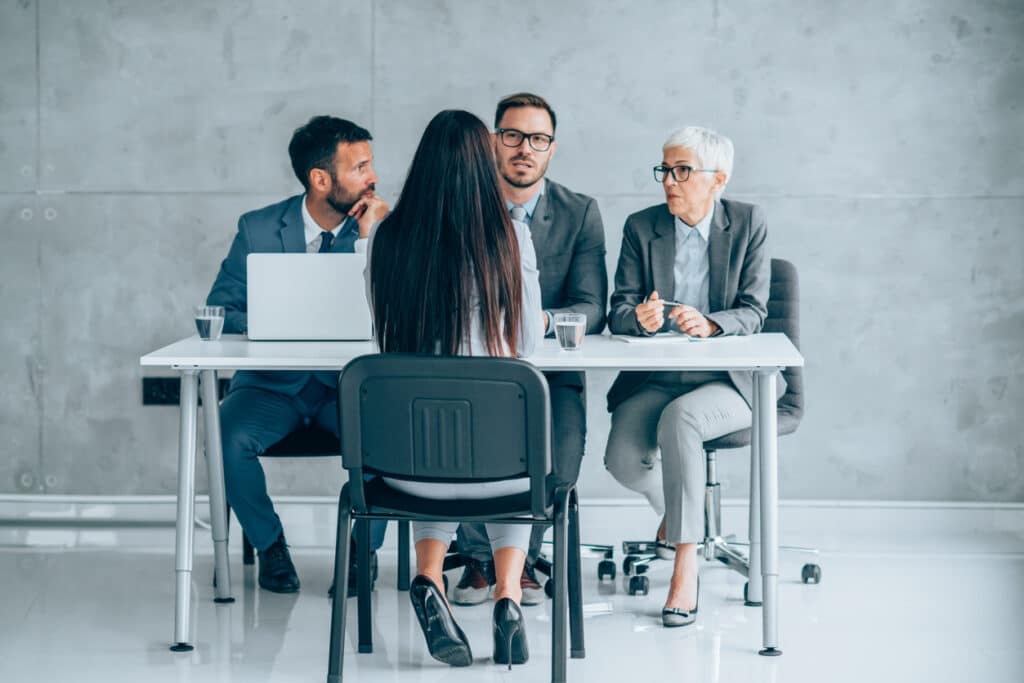 Shot of a group of businesspeople interviewing a female candidate in an office. Back view of young businesswoman during job interview in modern office.