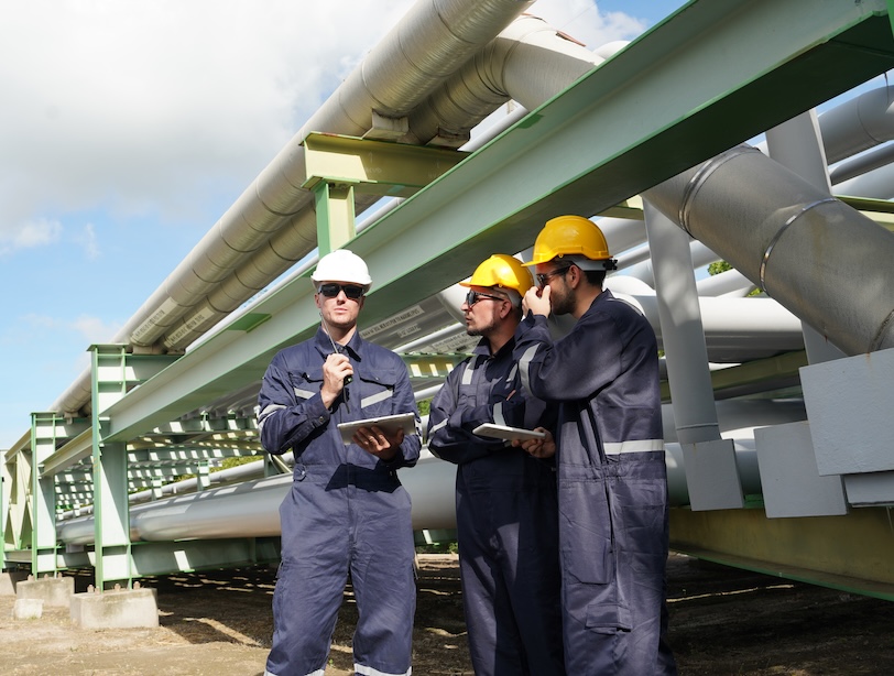 three male engineers in Uniform Holding stand to talk to check Gas Leakage Pipe System and Maintenance System and Training Oil Refinery at Column Tank Oil of Petrochemistry Industry.