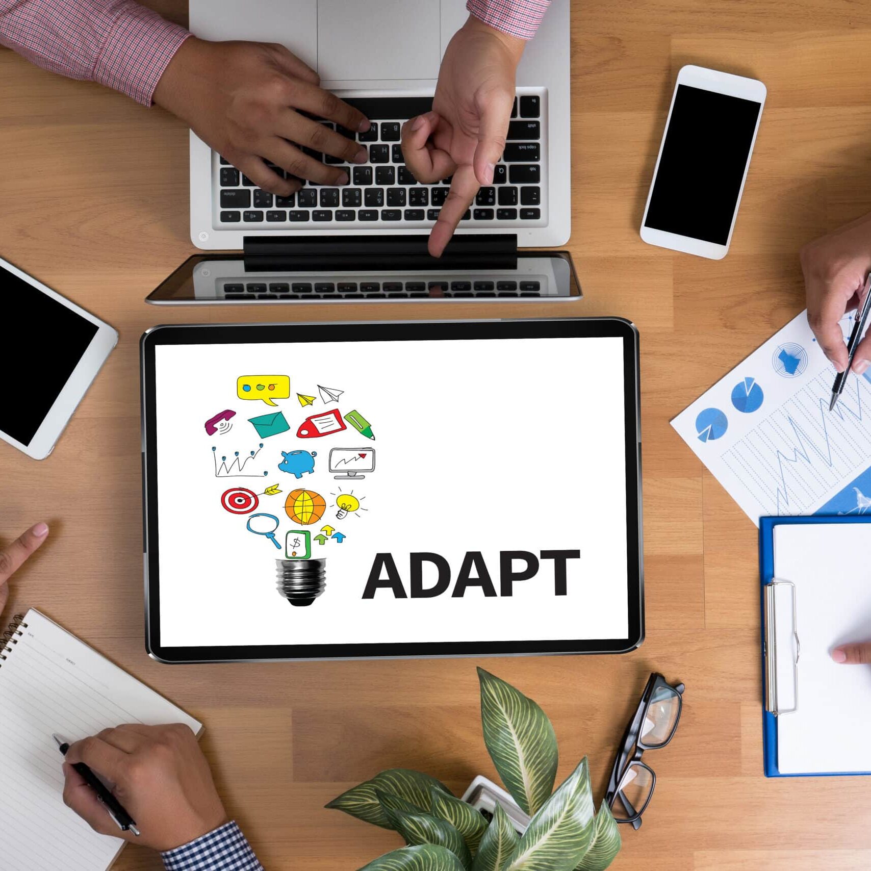 ADAPT Business team hands at work with financial reports and a laptop, top view