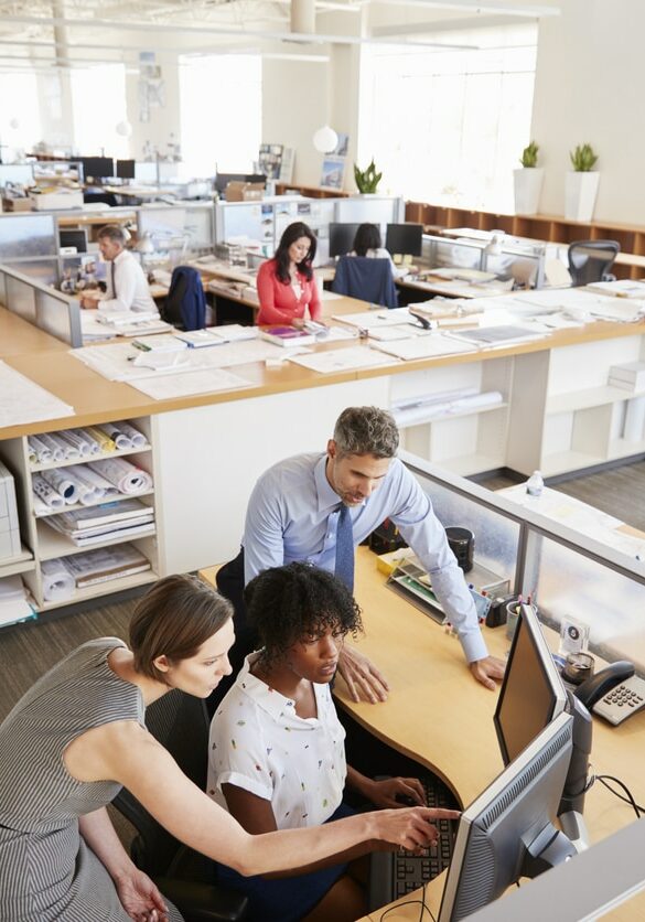 Colleagues working at a womanâ"u20acs workstation in a busy office